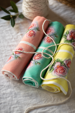 A set of rolled up linen tea towels with rose and three colours, pink, green, yellow.
